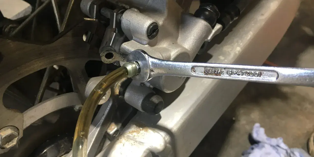 Klucz nasadowy odkręca odpowietrznik podczas czyszczenia hamulców motocykla. Płyn hamulcowy spływa przez przezroczysty wężyk.