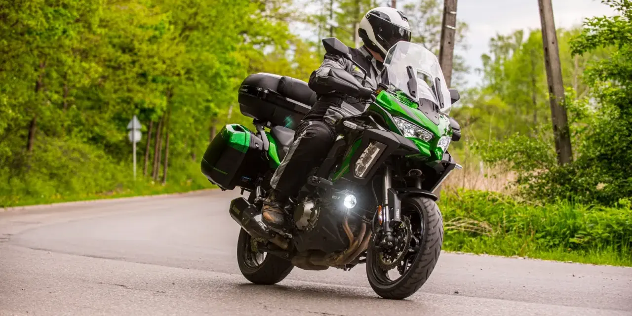 Motocyklista na zielonym Kawasaki Versys 1000, z kuframi, pokonuje zakręt. Nawet z potencjalnymi wadami, jazda nim to przygoda.