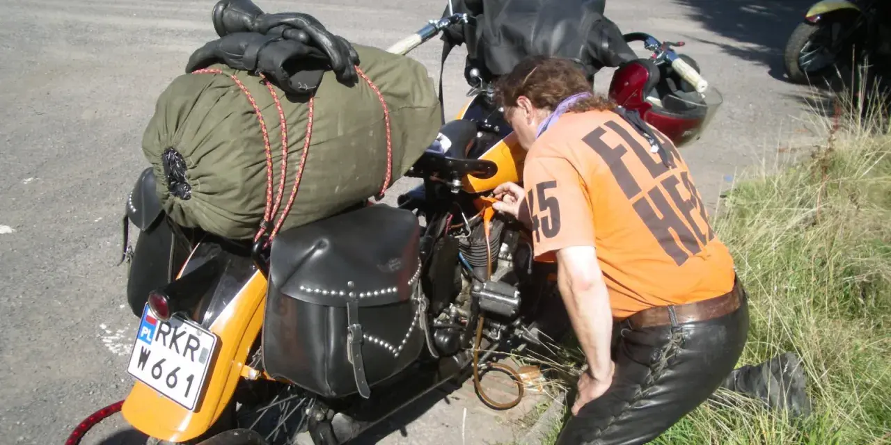 Motocyklista sprawdza uszkodzony gaźnik objawy. Na motocyklu sakwy, zielony worek i czarne rękawice.