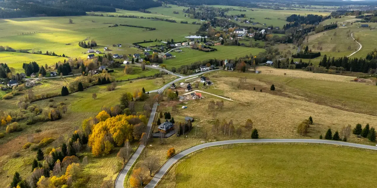 Malownicza autostrada sudecka wijąca się przez jesienne krajobrazy, pola i lasy. W oddali widać zabudowania wsi.