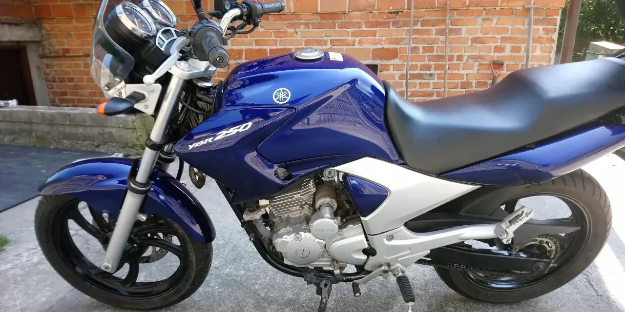 Błękitny motocykl Yamaha YBR 250 z chromowanymi elementami, zaparkowany na tle ceglanej ściany.