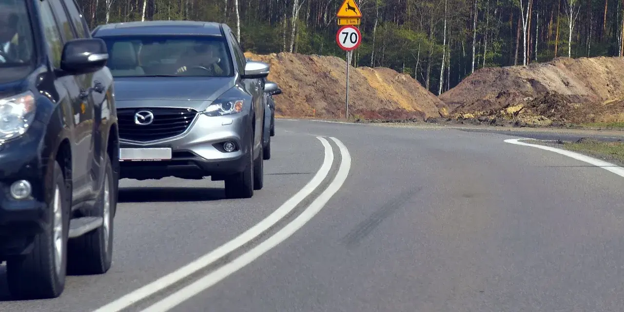 Kierowca próbuje wyprzedzanie na podwójnej ciągłej, ignorując znak ograniczenia prędkości do 70 km/h i ostrzeżenie o dzikich zwierzętach.