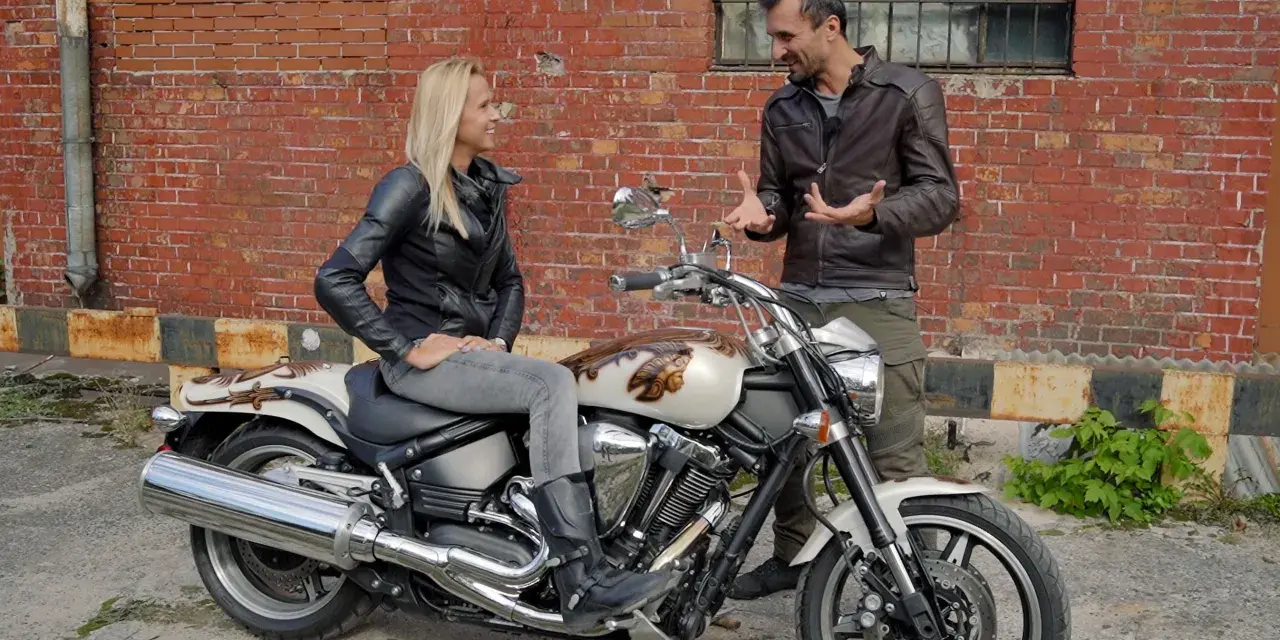 Kobieta siedzi na motocyklu Yamaha Warrior 1700, mężczyzna obok opowiada o jego możliwościach.