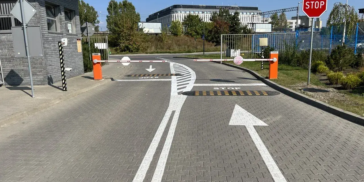 Przed wjazdem na teren, gdzie obowiązuje znak P-15, stoją szlabany. Na drodze namalowano strzałki kierunkowe i napis STOP.
