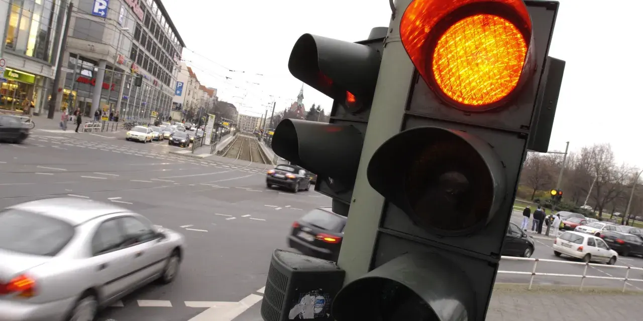 Żółte światło na sygnalizatorze drogowym, ruch uliczny i budynki w tle.