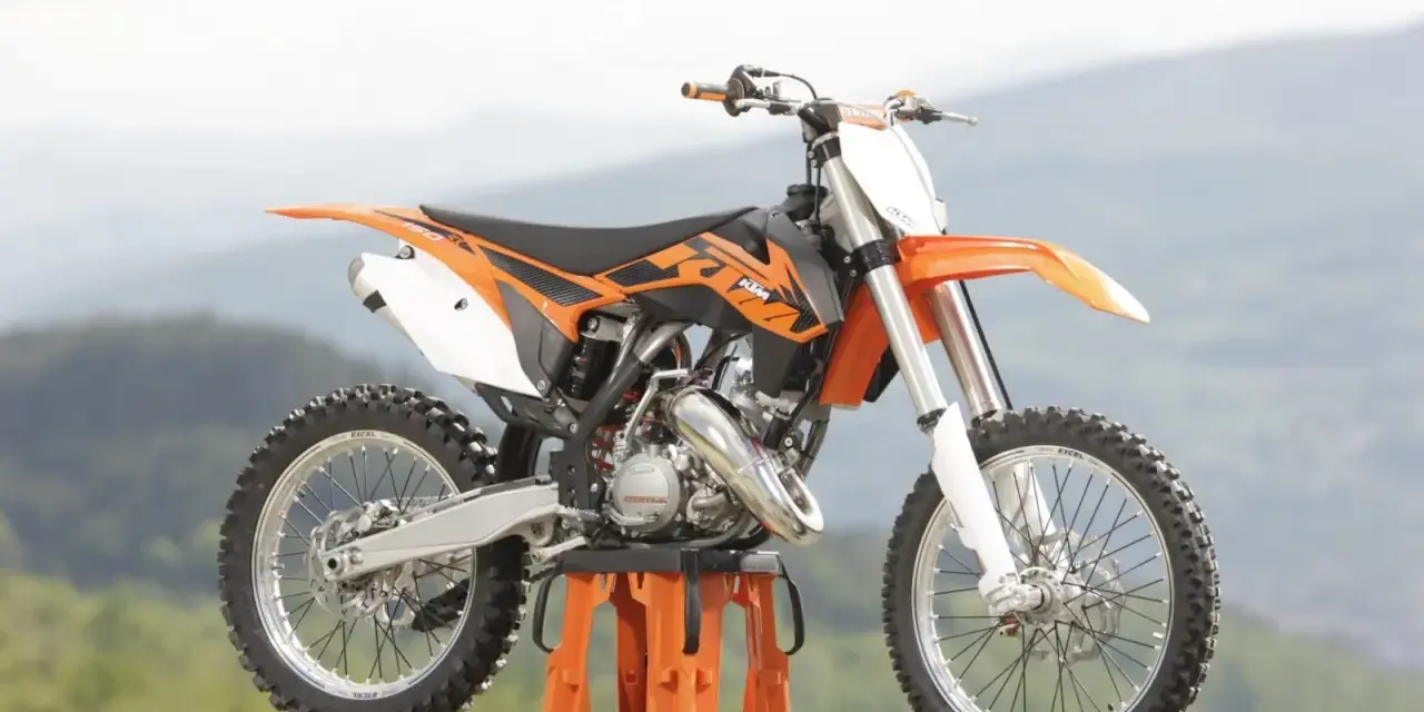 Pomarańczowy KTM SX 125 gotowy do osiągnięcia v-max na górskich trasach.