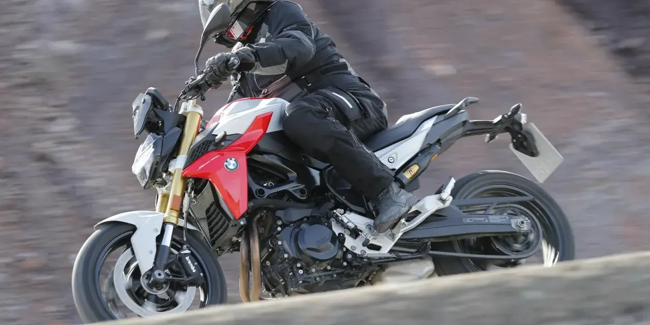 Motocyklista w kasku i kombinezonie pędzi na motocyklu BMW F900R po kamienistym terenie.