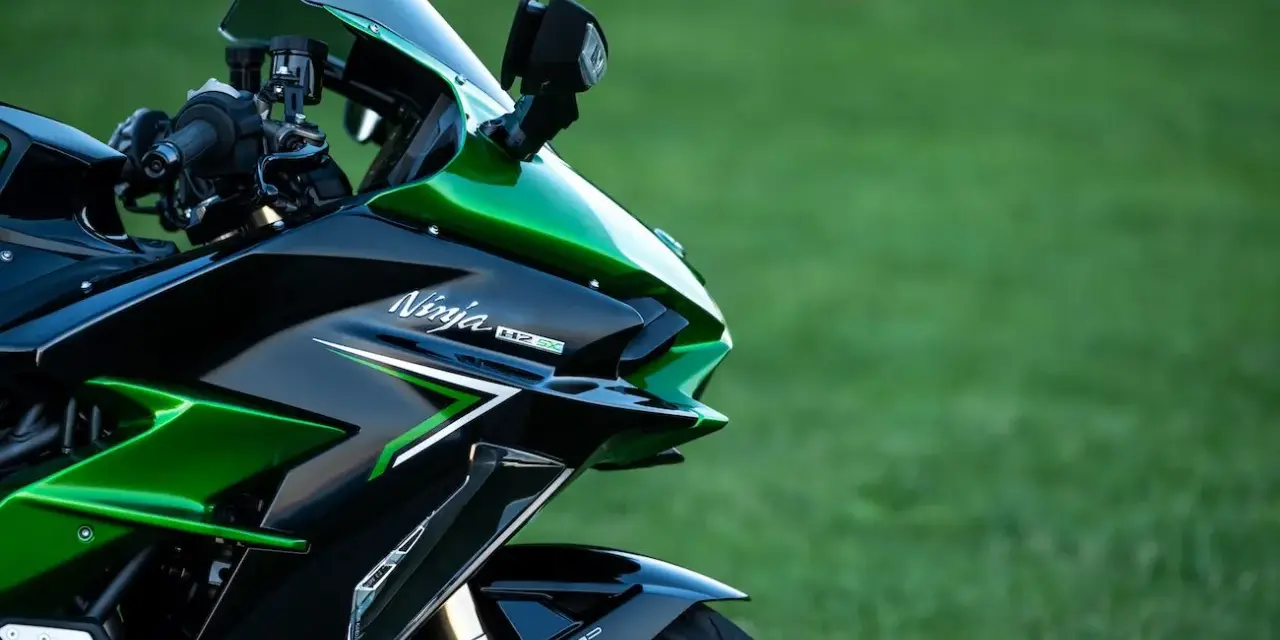 Błyszczący, czarno-zielony motocykl Kawasaki H2 SX z napisem "Ninja H2 SX" na owiewce, zaparkowany na tle zielonej trawy.