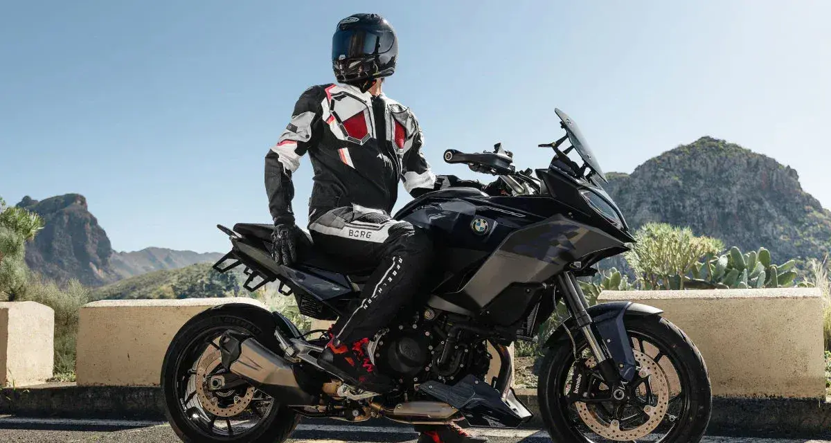 Motocyklista w kombinezonie na czarnym motocyklu BMW, gotowy do podróży po górskich drogach. Wśród wielu marek motocykli, ta prezentuje się imponująco.
