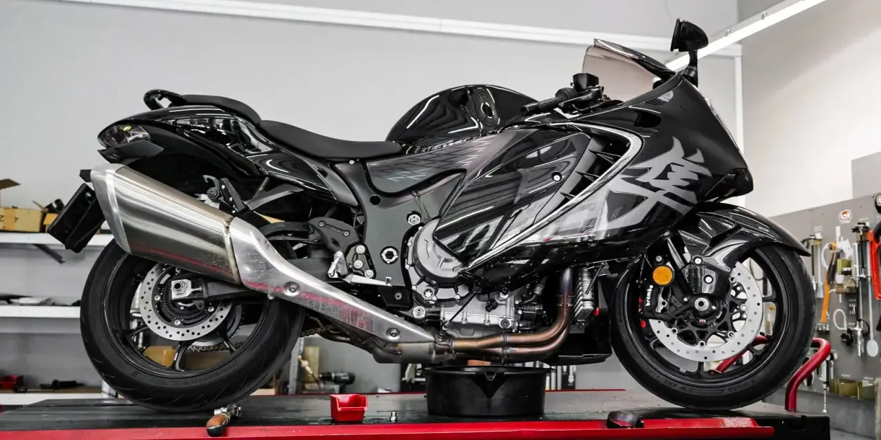 Czarny motocykl na podnośniku, gotowy do serwisu. Widać duży, chromowany wydech, który odcina się od reszty maszyny.