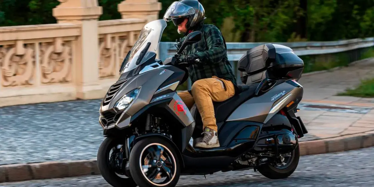 Mężczyzna w kasku jedzie trójkołowym skuterem Peugeot Metropolis 400. Widoczna jest jego prędkość maksymalna.