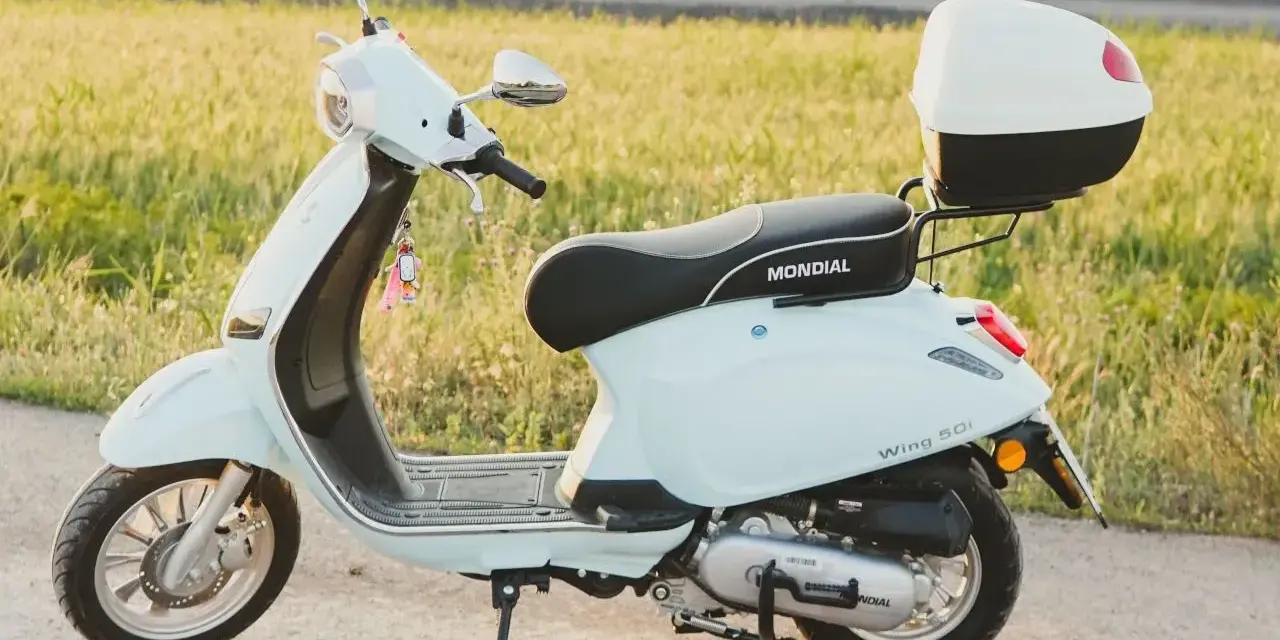 Jasny skuter Mondial Wing 50i, idealny na pierwsze przejażdżki bez prawa jazdy, stoi na tle zielonego pola.