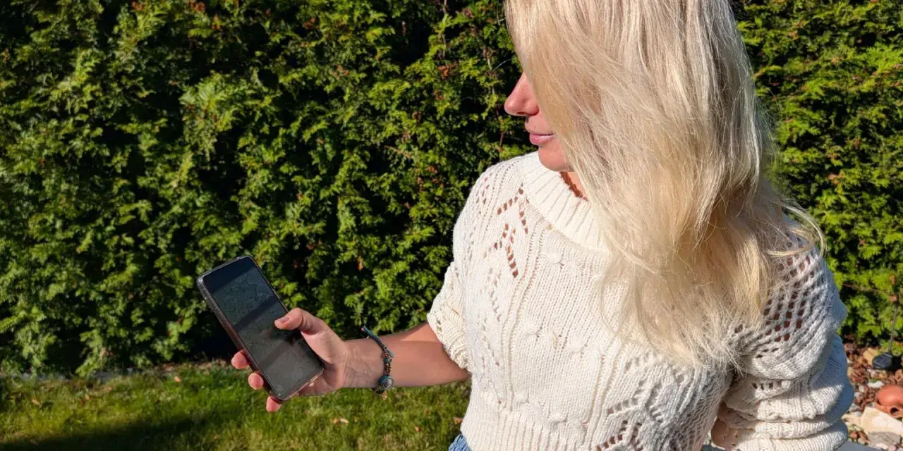 Blondynka w białym swetrze korzysta z telefonu, by wyznaczyć trasę krok po kroku.