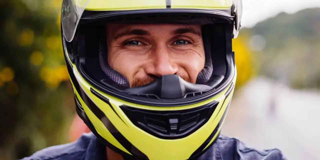 Uśmiechnięty mężczyzna w żółtym kasku motocyklowym.