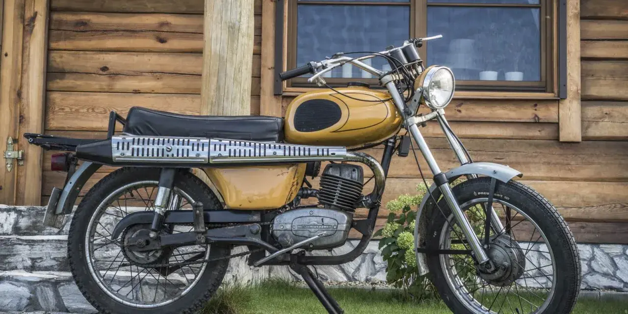 Żółty motorower WSK 175, z widocznymi danymi technicznymi na silniku, stoi przed drewnianym domem.