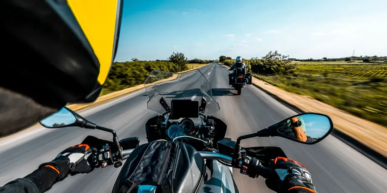 Przełęcz Salmopolska widziana z perspektywy motocyklisty. Droga wijąca się pośród zielonych pól, błękitne niebo i inny motocykl przed nami.