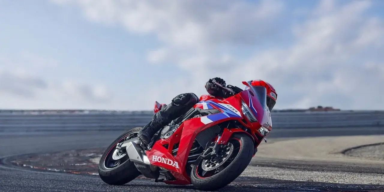 Czerwony motocykl Honda CBR650R z kierowcą pochylonym na zakręcie toru wyścigowego.