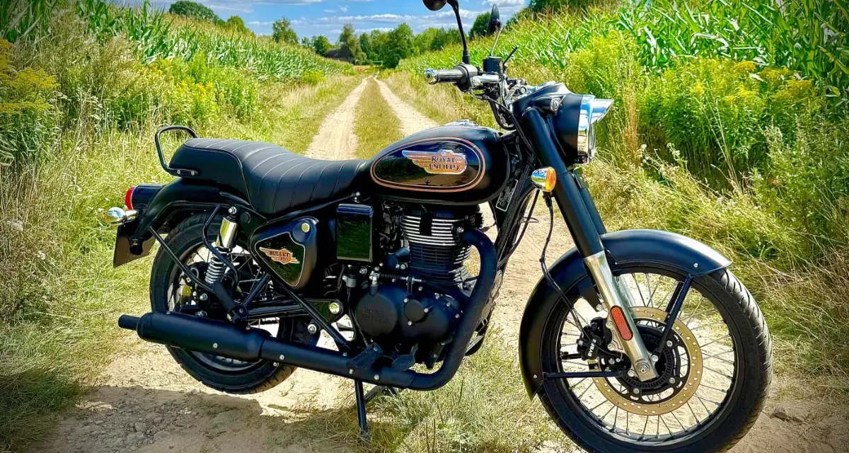Czarny motocykl Royal Enfield Diesel na polnej drodze, otoczony zielenią i kukurydzą.