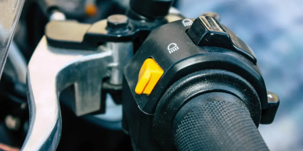 Pomarańczowy przycisk na kierownicy motocykla, który może służyć jako kill switch, obok przełącznika świateł.