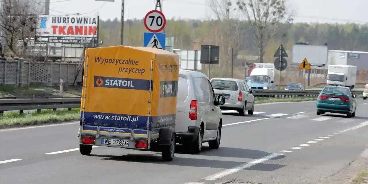 Samochód z przyczepą Statoil jedzie drogą. Znak ograniczenia prędkości 70 km/h sugeruje, ile można jechać na autostradzie w tym miejscu.