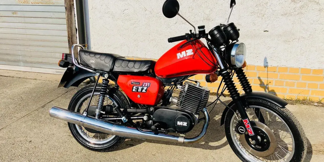 Czerwony motocykl MZ ETZ 251 z lat 80. stoi przed garażem.