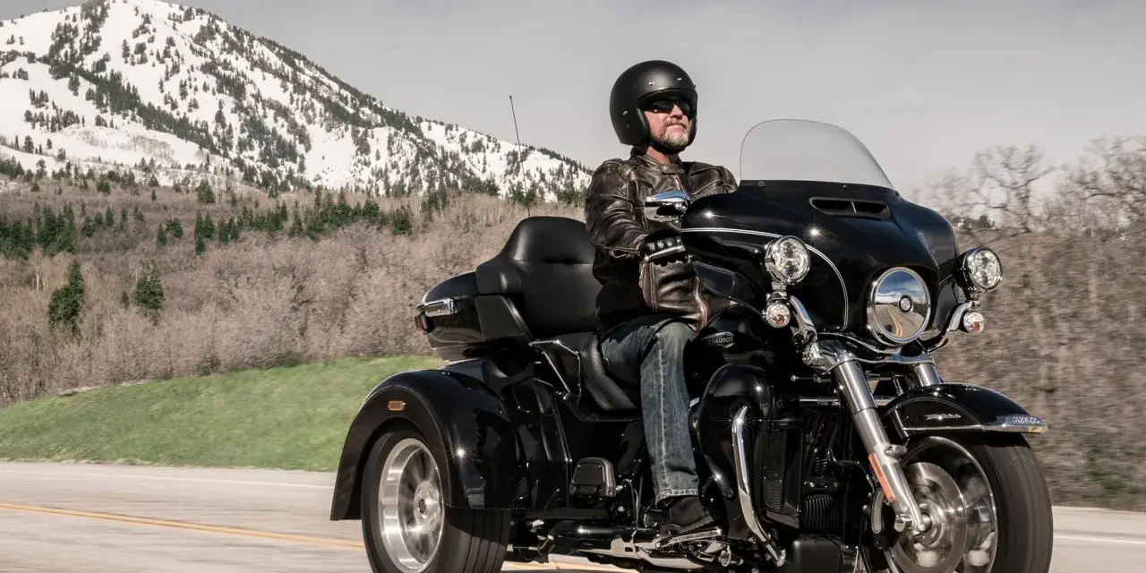 Mężczyzna w kasku i skórzanej kurtce jedzie czarnym motocyklem trójkołowym L5E. W tle góry ze śniegiem.