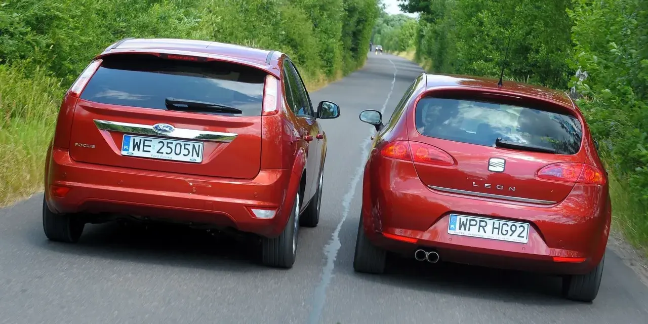 Dwa czerwone auta jadą drogą. Jedno z nich, Ford Focus, próbuje omijanie, podczas gdy Seat Leon wykonuje wymijanie.