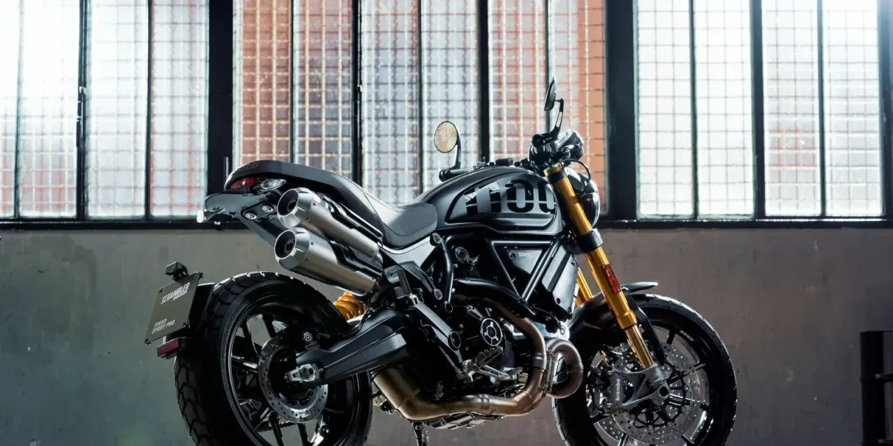 Czarny motor scrambler z podwójnym wydechem i złotym zawieszeniem, gotowy do jazdy po miejskich ulicach.