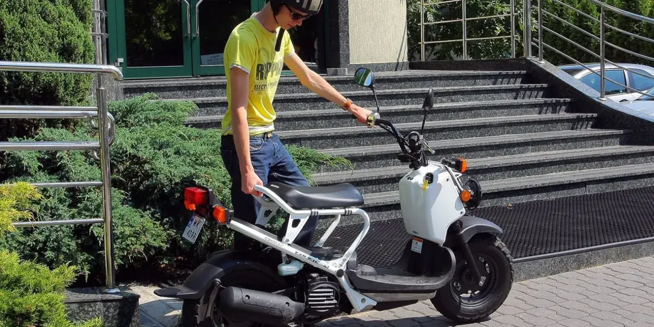 Młody mężczyzna w kasku i żółtej koszulce przy białym skuterze. To jego stara karta motorowerowa, gotowa do jazdy.