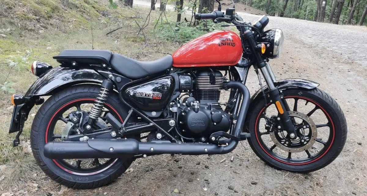 Czerwony Royal Enfield Meteor 350 na leśnej drodze. Klasyczny wygląd i gotowość do podróży.