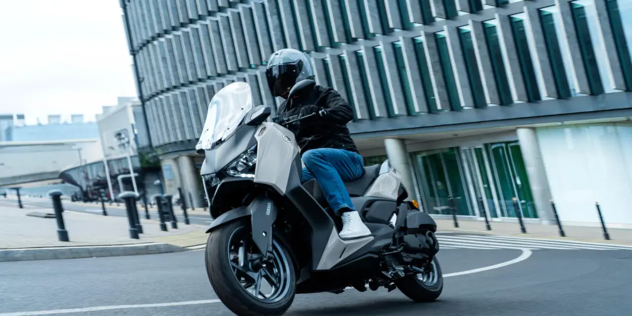 Mężczyzna w kasku jedzie skuterem Yamaha X-MAX 125 po mieście. Czy to lepszy wybór niż Honda Forza 125?