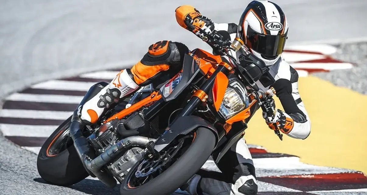Motocyklista w kombinezonie ściga się na torze na pomarańczowym KTM 1290 Super Duke, pochylony w zakręcie.