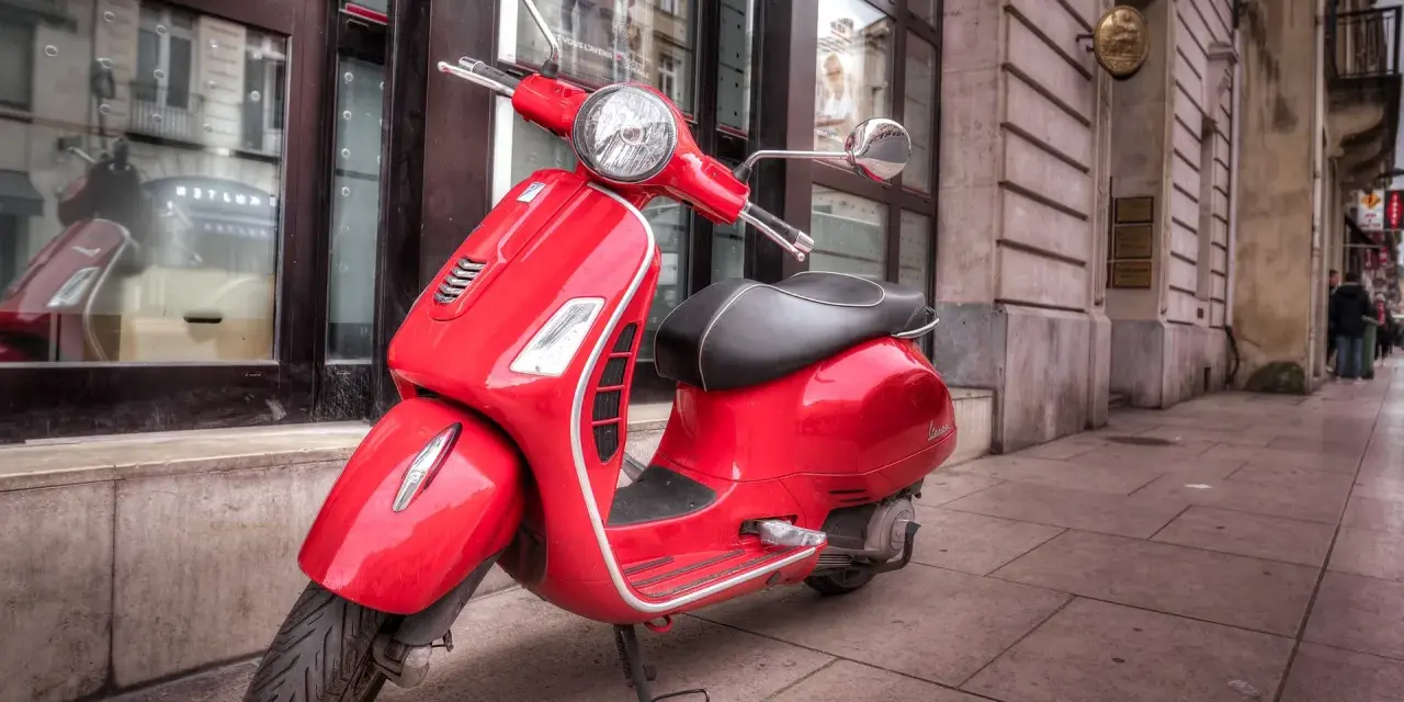 Czerwony skuter Vespa, idealny do miasta. Marzenie o posiadaniu go jest jak marzenie o zdobyciu prawa jazdy na skuter.