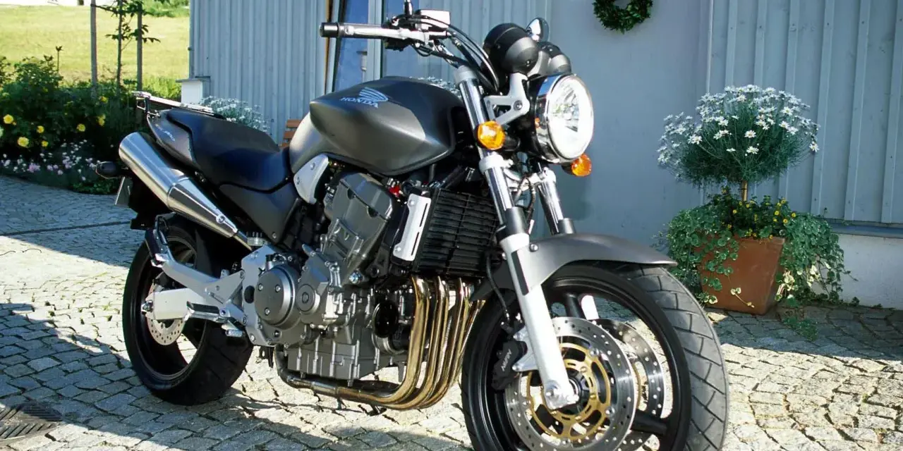 Szary motocykl Honda 919 zaparkowany na bruku przed domem.