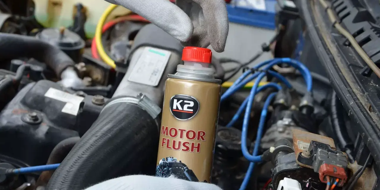 Ręka w rękawiczce trzyma puszkę płukanki do silnika motocyklowego K2 Motor Flush, gotowa do użycia w silniku.