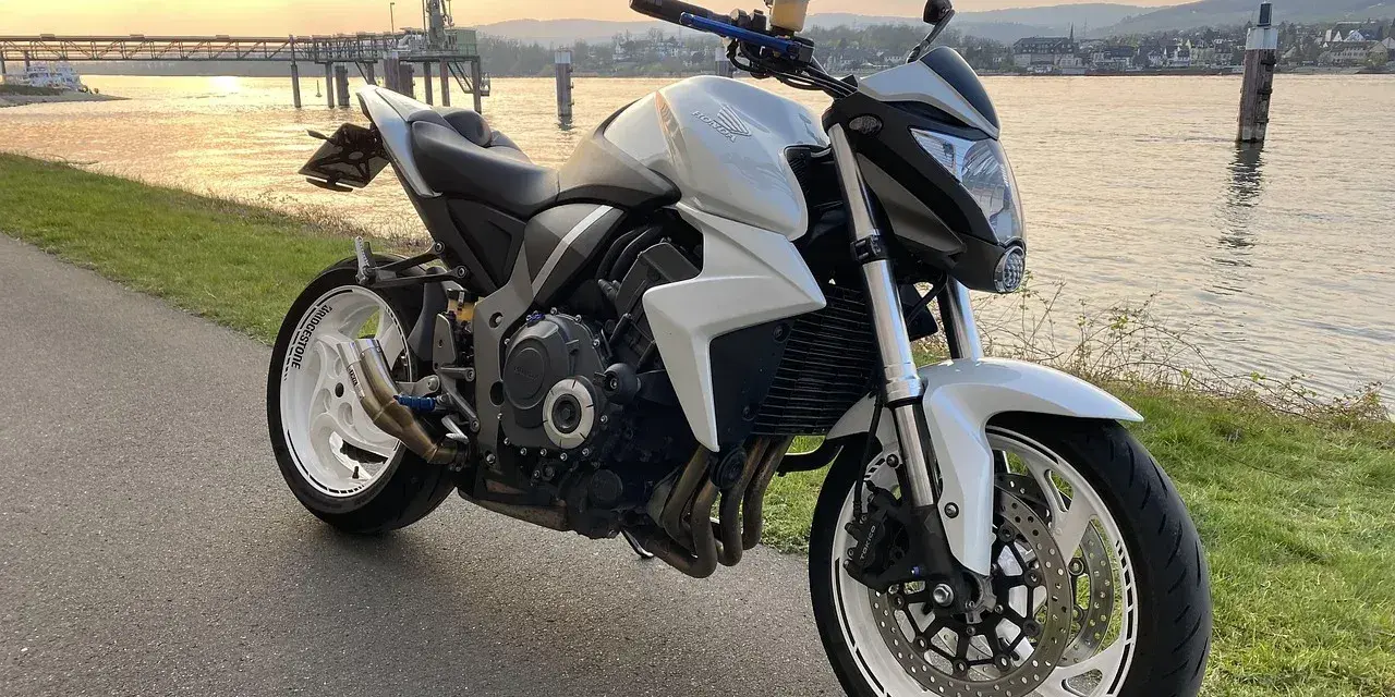 Biały motocykl Honda z silnikiem 35 kw nad rzeką o zachodzie słońca.