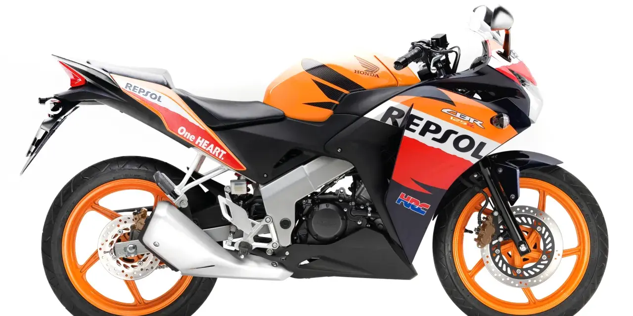 Pomarańczowo-czarny motocykl Honda CBR 125R w barwach Repsol, gotowy do wyścigów.