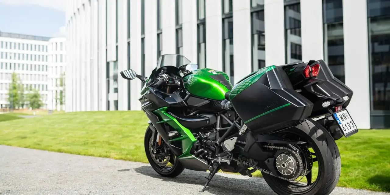 Zielony Kawasaki Ninja H2 z czarnymi kuframi, gotowy do podróży obok nowoczesnego budynku.