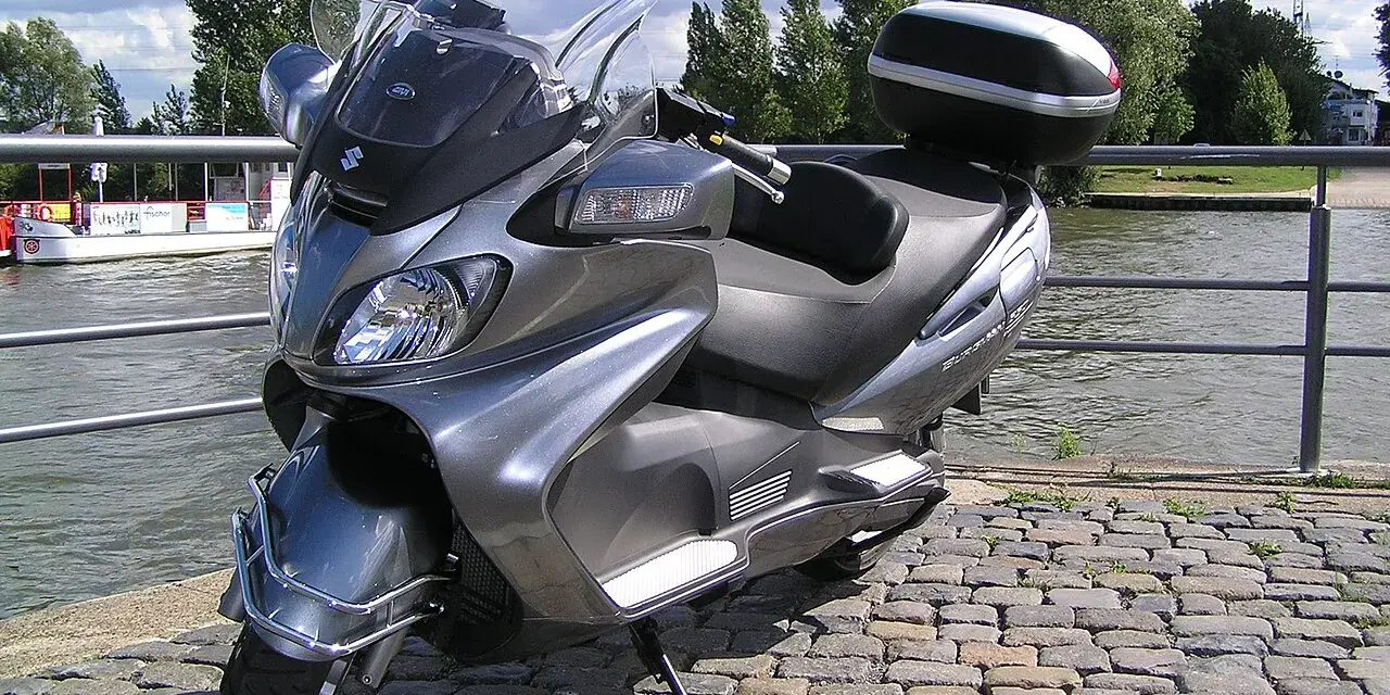 Szary Suzuki Burgman 650, gotowy na podróż w stylu V-max, stoi nad wodą.