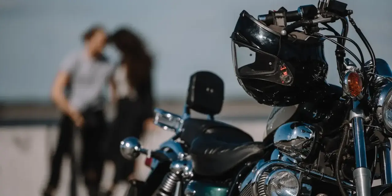Motocykl z kaskiem na kierownicy, w tle para w czułym uścisku. Idealny dzień na wspólną podróż 4t.
