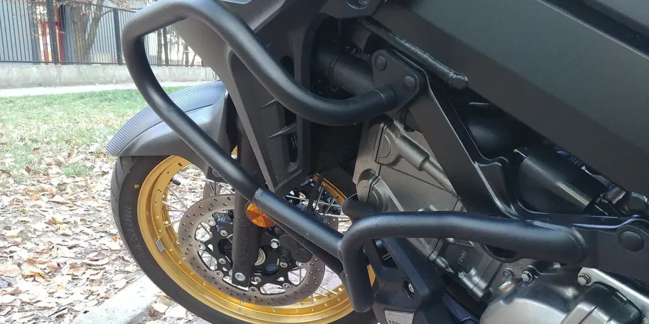 Żółty motocykl z czarnymi gmolami chroniącymi silnik i osłony. Złota obręcz koła i tarcza hamulcowa.