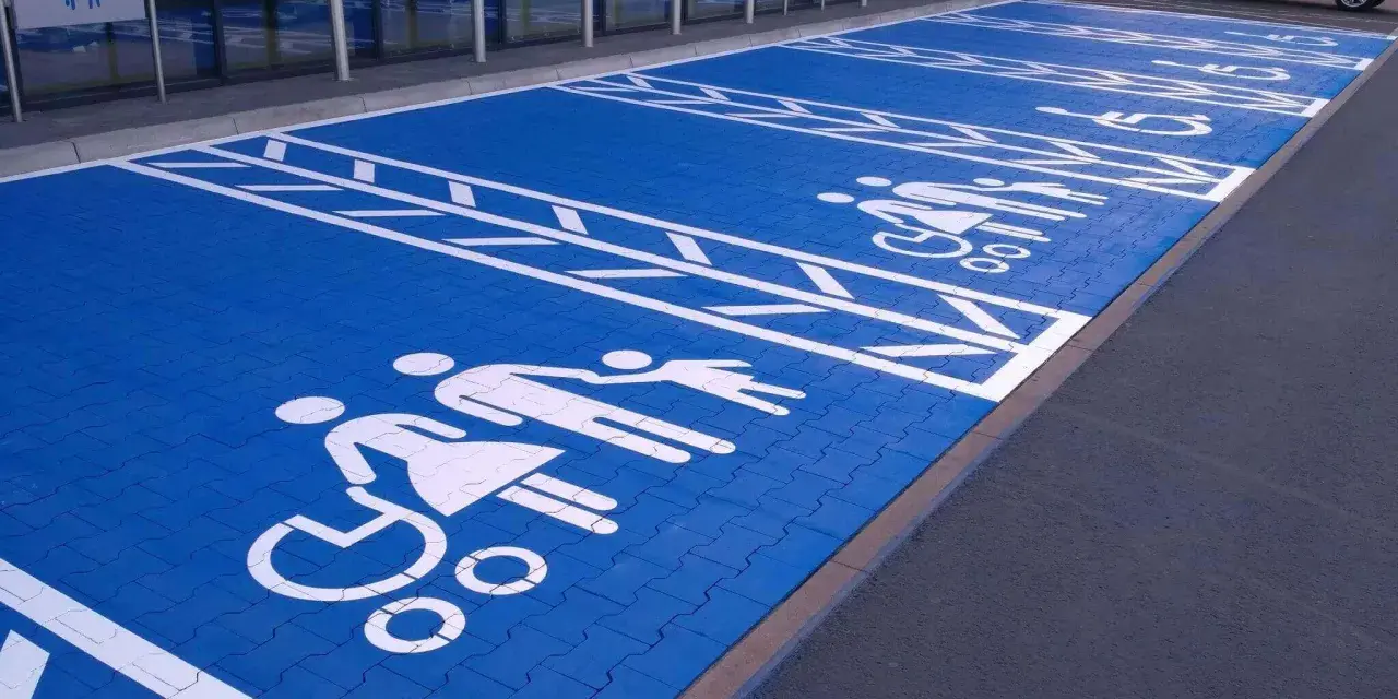 Niebieski parking z białymi symbolami osób na wózkach inwalidzkich i rodzin. Znak P19 informuje o przeznaczeniu miejsc.