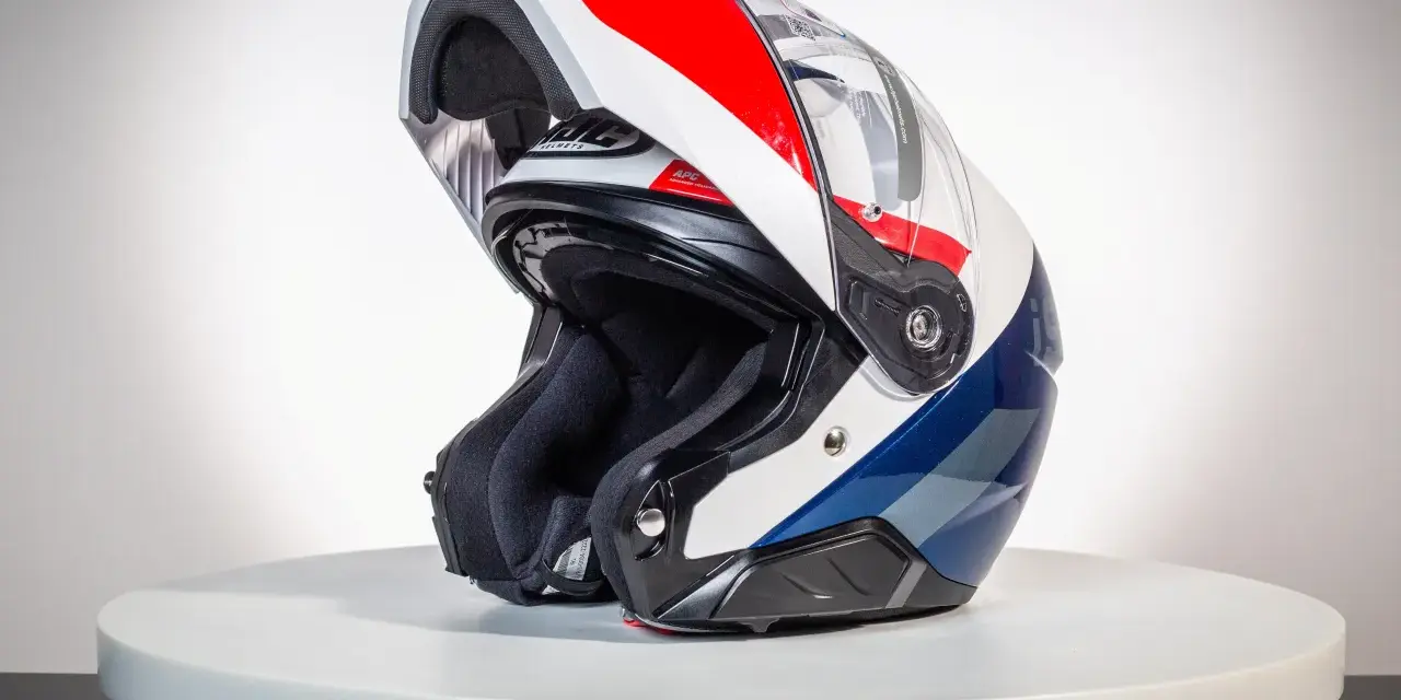 Kask motocyklowy z podniesioną szczęką, w kolorach białym, czerwonym i niebieskim, na białym tle.