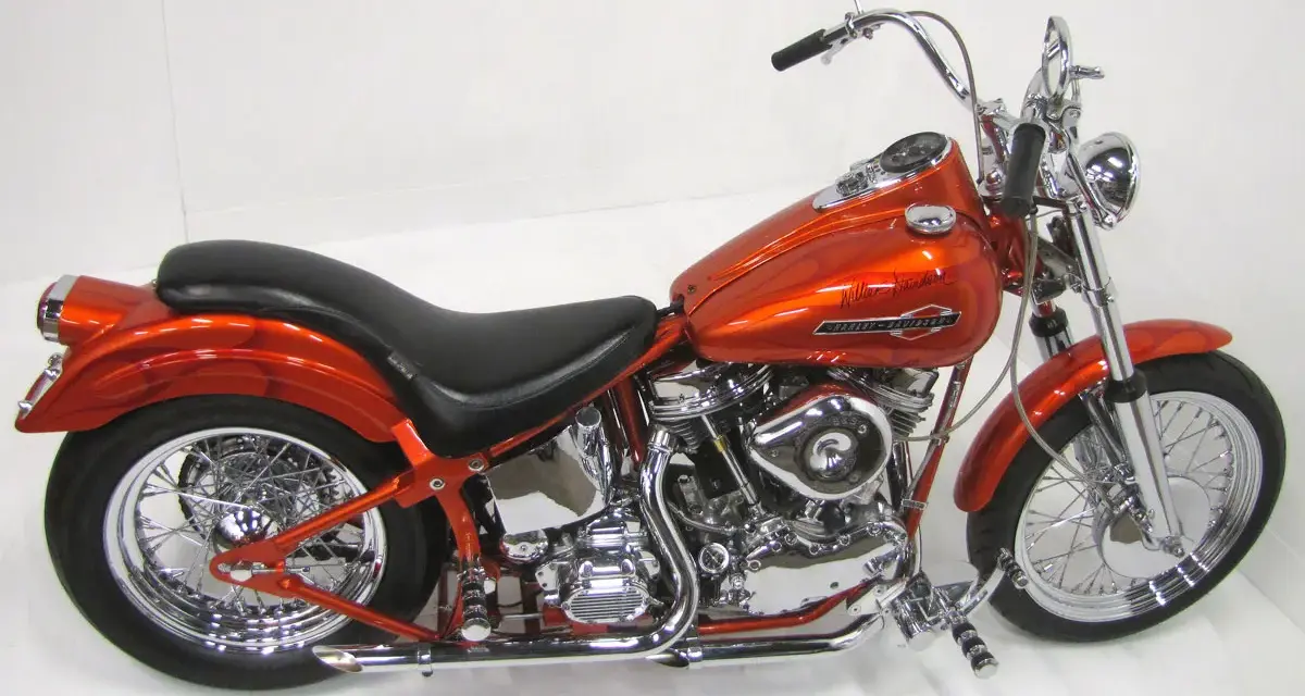 Pomarańczowy motocykl Harley-Davidson z silnikiem panhead, błyszczący chrom i płomienie na baku.
