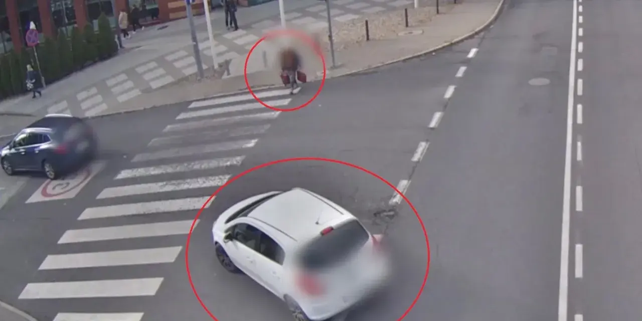 Biały samochód wymusza pierwszeństwo na pasach, omal nie potrącając pieszego z walizką. Inny samochód zatrzymał się przed przejściem.