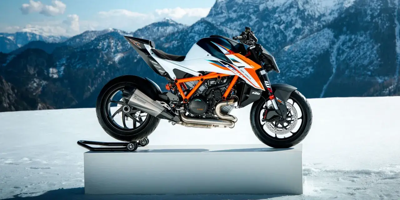 Pomarańczowo-biały KTM Super Duke na śnieżnym tle z górami w tle.