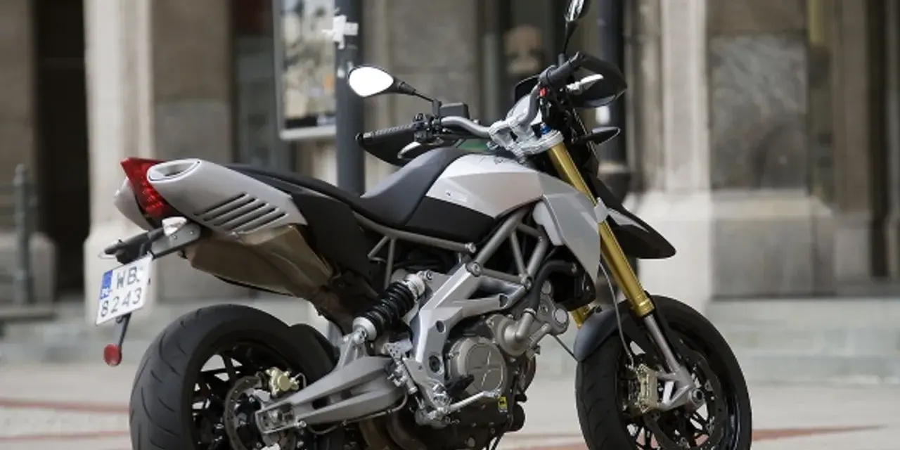Srebrno-czarny motocykl Aprilia Dorsoduro 750 z żółtymi amortyzatorami, gotowy do jazdy po miejskich ulicach.