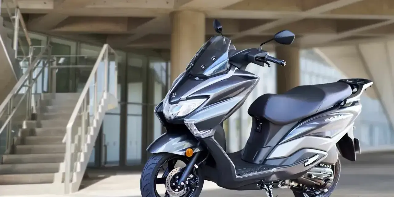 Szary skuter Suzuki Burgman 125 na tle nowoczesnego budynku z betonowymi schodami.