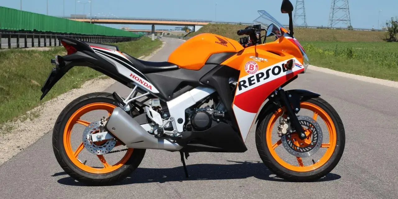 Pomarańczowy motocykl Honda CBR 125 Repsol na drodze. Warto sprawdzić honda cbr 125 dane techniczne przed zakupem.