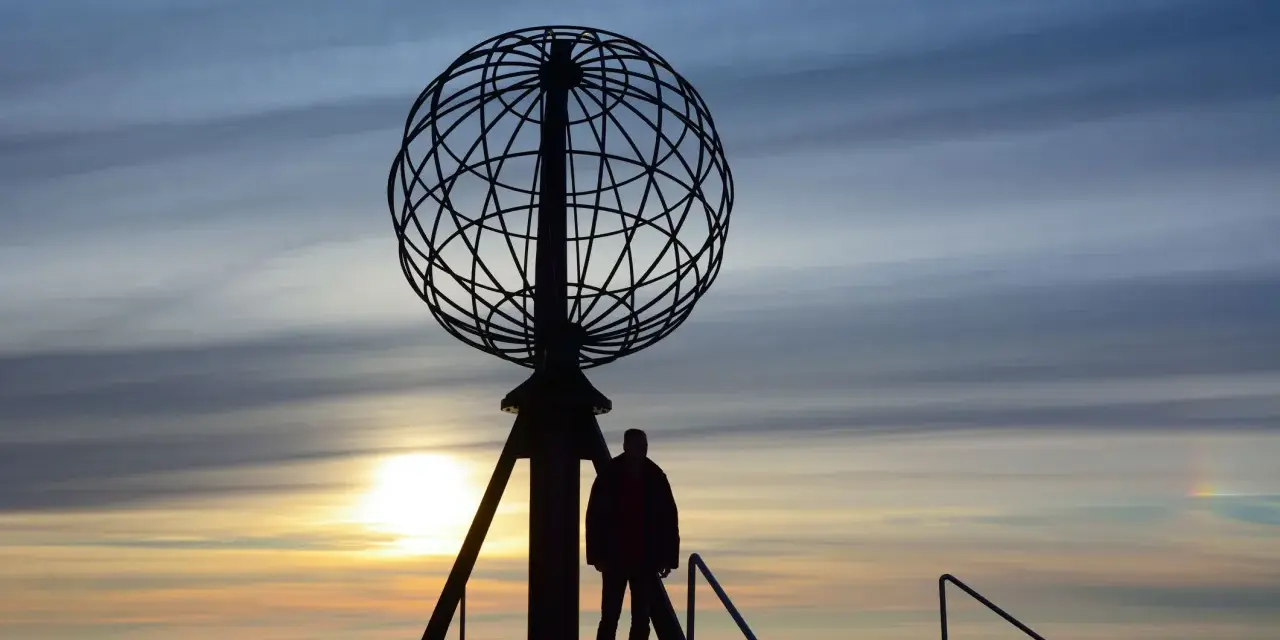 Sylwetka człowieka przy globusie na Nordkapp podczas zachodu słońca.